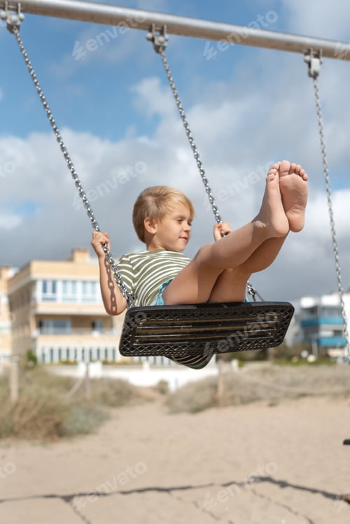 Preview: A boy on a swing on a sandy beach against the backdrop of apartment buildings and a stormy sky.