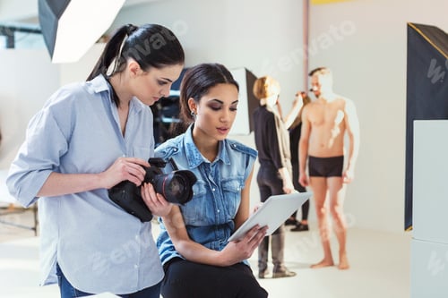 Preview: Fashion model and photographer reviewing shoot on digital tablet in photography studio