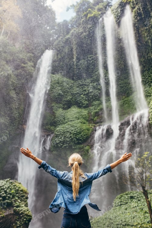 Preview: Excited woman standing by waterfall