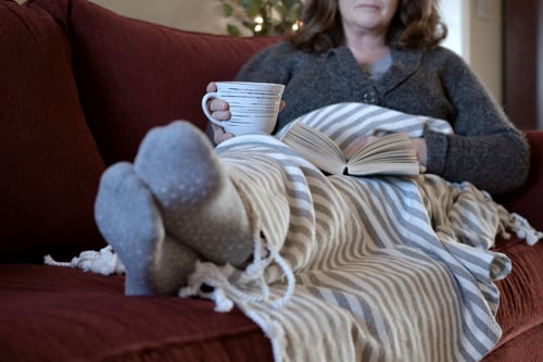 Mujer descansando en el sofá (sofá) con una taza caliente de té o café mientras lee un libro.