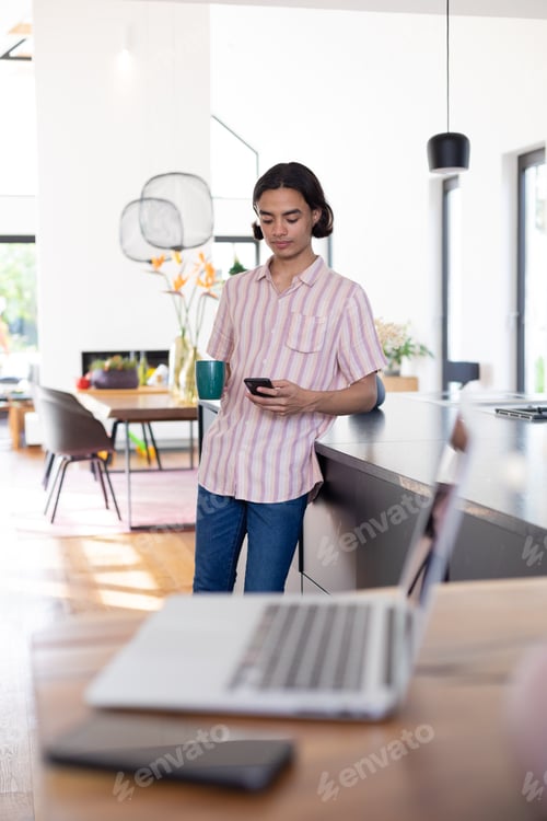 Preview: Happy biracial man using smartphone in kitchen