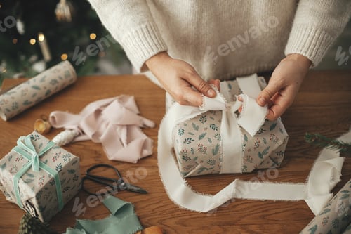 Preview: Woman wrapping christmas gift with stylish ribbon on wooden table