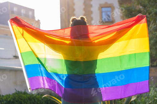 Preview: A closeup shot of a young Caucasian female silhouette behind LGBT pride flag outdoors