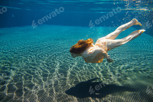 Preview: Businesswoman swimming underwater in elegant clothes in a pool