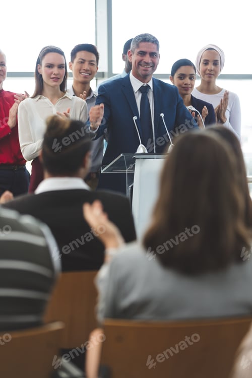 Preview: Businessman standing on podium with diverse colleagues while he speaks at business seminar in office