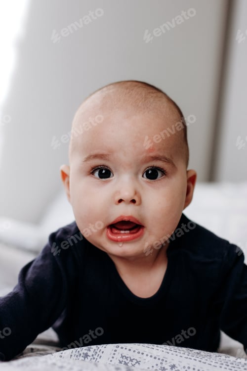 Preview: Sweet chubby cheeky baby boy lying on his tummy on the bed.