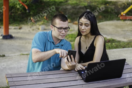 Preview: Two young students sitting in the park talking and studying on the smartphone