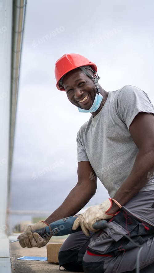 Preview: Afro-American craftsman drilling a wall with a drill machine and smiling