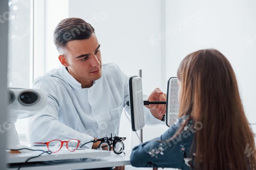 Preview: Two panels on the table. Young ophthalmologist is with little female visitor in the clinic