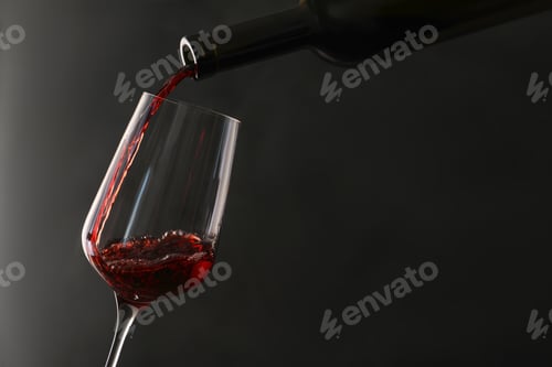 Preview: Pouring red wine from bottle into glass on dark background. Space for text