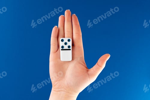 Preview: Woman hand holding domino piece against blue background, top view