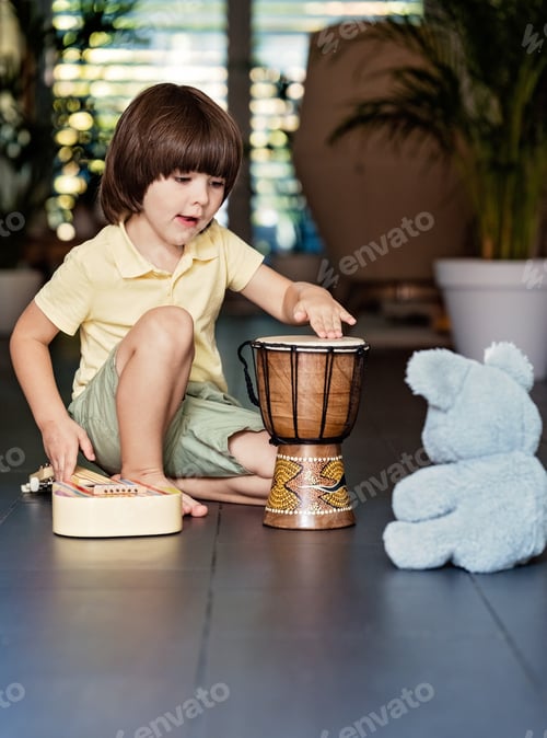Preview: Little toddler boy playing music on guitar and traditional African ethnic djembe drum at home