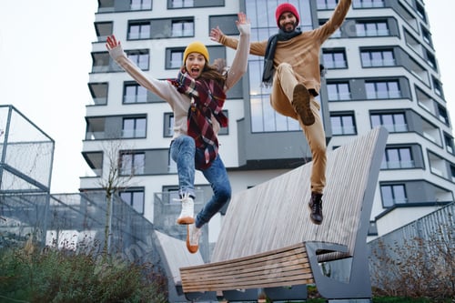 Preview: Cheerful young couple owners jumping outdoors in front of new flat, new home and relocation concept.