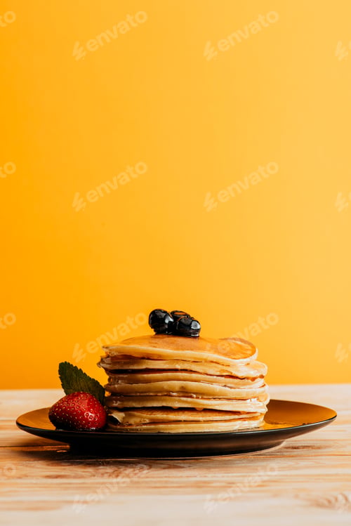 Preview: stack of delicious pancakes with berries on yellow