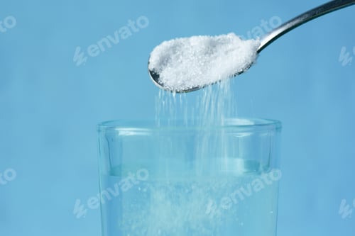 Preview: pouring white sugar in a glass of water on table