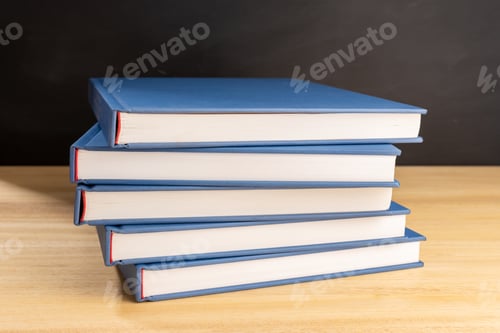 Preview: Pile of books on wooden table and black chalkboard at background