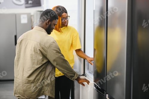 Preview: Young african american couple, satisfied customers choosing fridge in appliances store