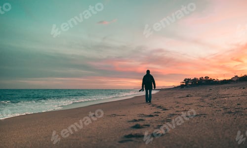 Preview: Fisherman walks on the sand by the sea at sunset.