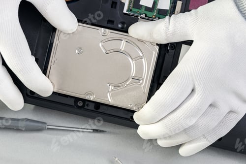 Preview: Technician hands removing an old mechanical hard disk from a laptop. Top view