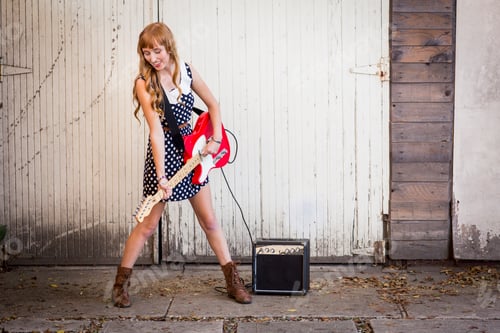 Preview: Young woman rocking out on an electric guitar in front of a rustic garage door.