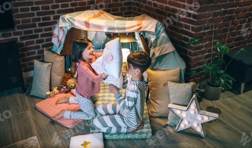 Preview: Happy siblings having fun in pillow fight on party at living room. Domestic family life concept.