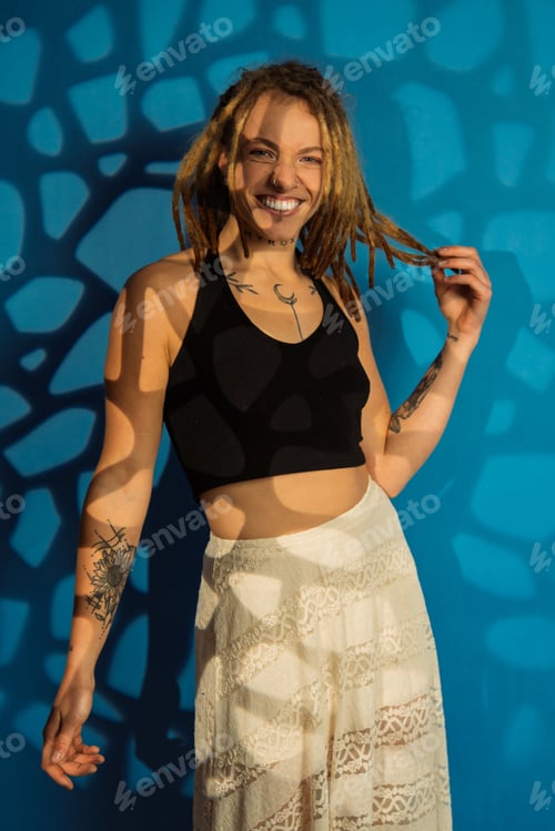 Preview: Young woman with dreadlocks smiling against blue wall