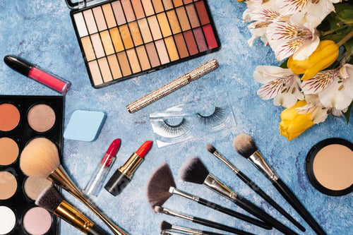 Preview: a set of decorative cosmetics, makeup brushes and a bouquet of flowers on a blue background