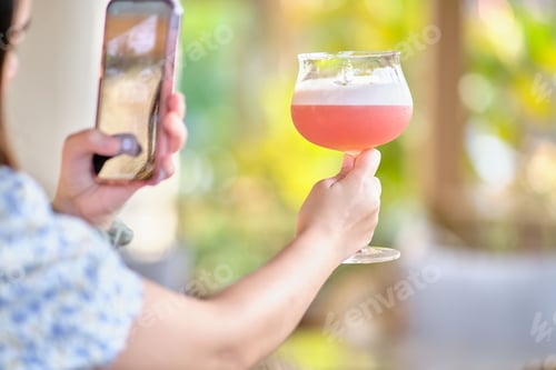 Preview: Female taking pictures of her pink cocktail in the outdoor bar