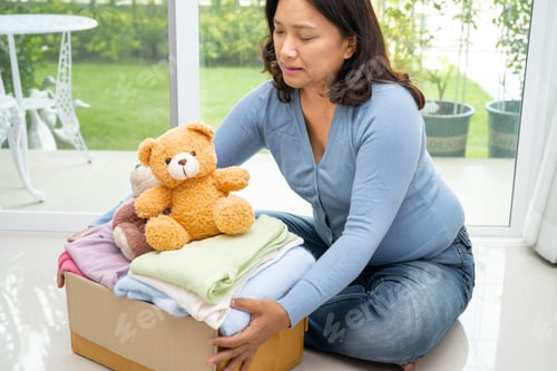 Preview: Holding clothing donation box with used clothes and doll at home to support help for poor people