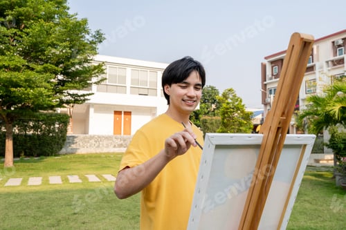 Preview: Asian young talented man artist coloring on painting board in park.