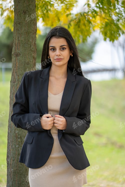 Preview: Young businesswoman holding her blazer in a park during autumn