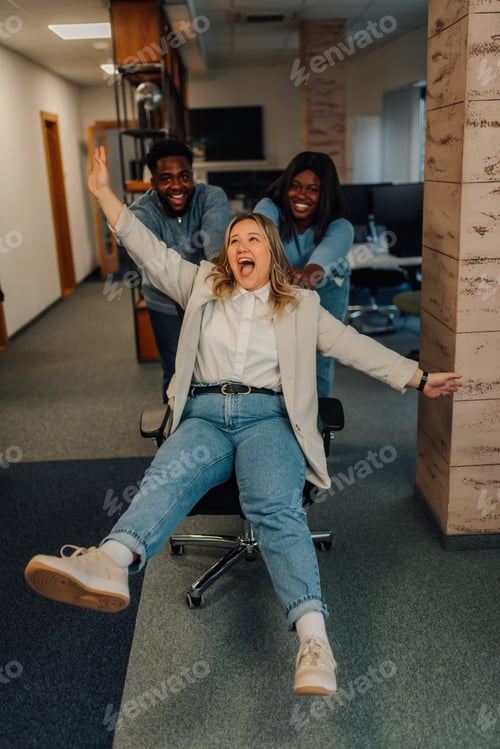 Preview: Business colleagues pushing businesswoman on office chair