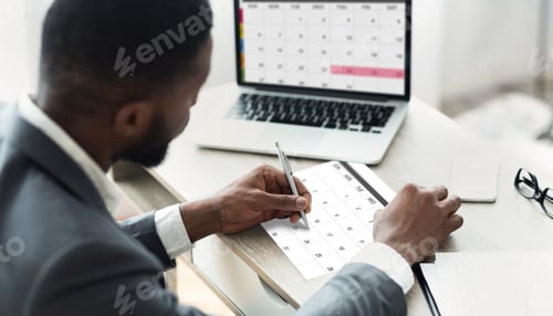 Preview: Black Businessman Using Calendar Program On Laptop And Writing Notes To Planner