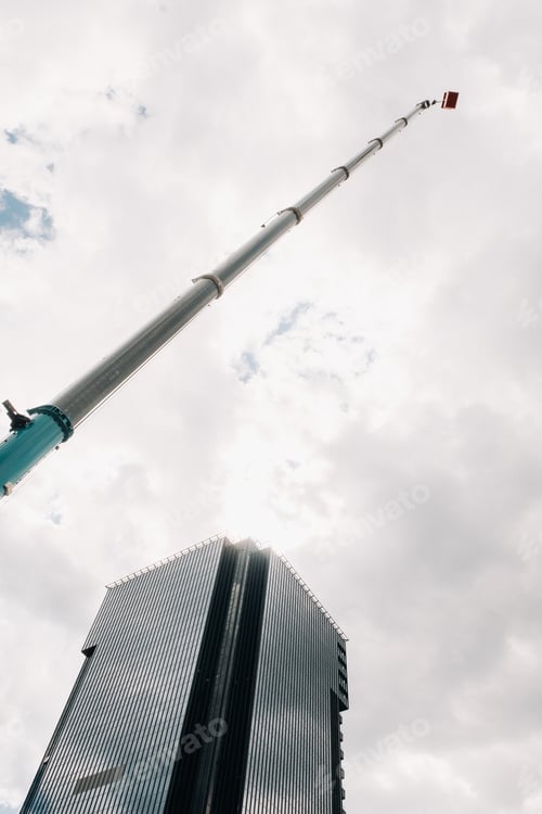 Preview: A large blue truck crane stands ready for operation on a site near a large modern building. The