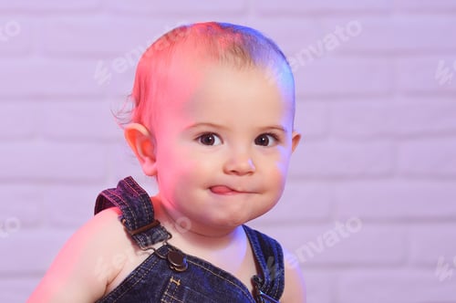 Preview: a portrait of a child boy in a denim overalls, which cunningly grimaces and shows the tongue.