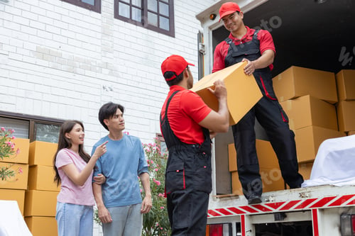 Preview: Young couple checks with two movers unloading boxes and furniture from a pickup truck
