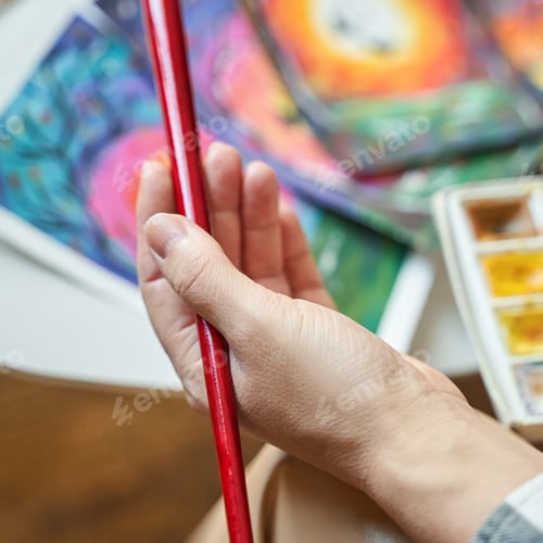 Preview: Female artists hand holding red brush with colorful paintings and watercolor