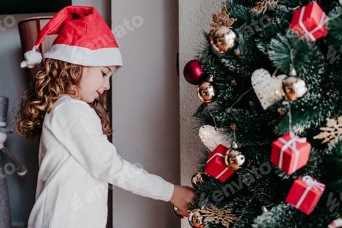 Visualização: menina criança decorando a árvore de natal em casa. Conceito de Natal. usando um chapéu de Papai Noel vermelho