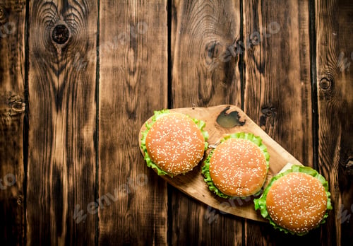 Preview: Three finished Burger with meat and vegetables on wooden stand.