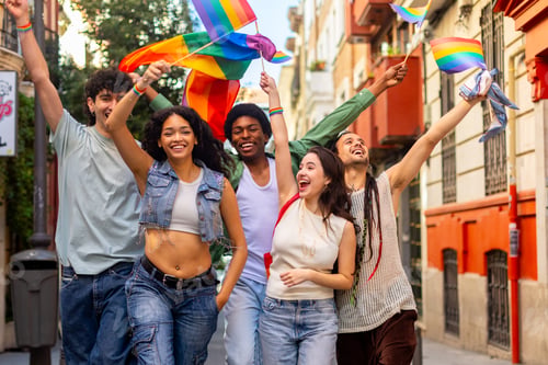 Preview: Happy multi ethnic friends waving rainbow flags celebrating gay pride in the city