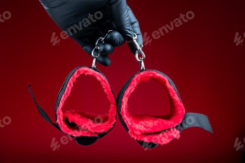 Preview: hands in black gloves holding handcuffs with red belts for bdsm sex games