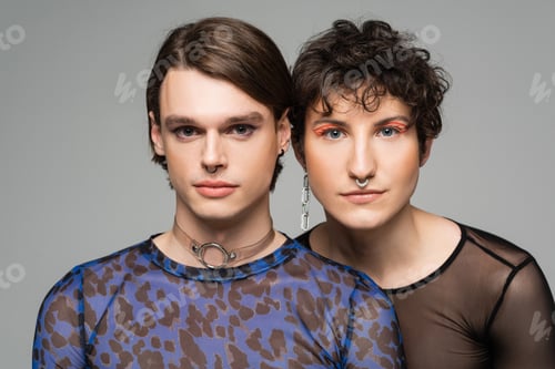 Preview: portrait of young and stylish pansexual couple with makeup looking at camera isolated on grey