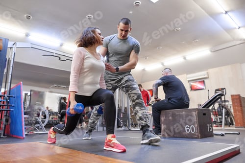 Preview: Personal fitness instructor helping summer woman exercising in health club.