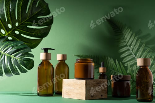 Preview: Bottles for cosmetics and cream on a pedestal, green background with leaves and shadow. Brown glass