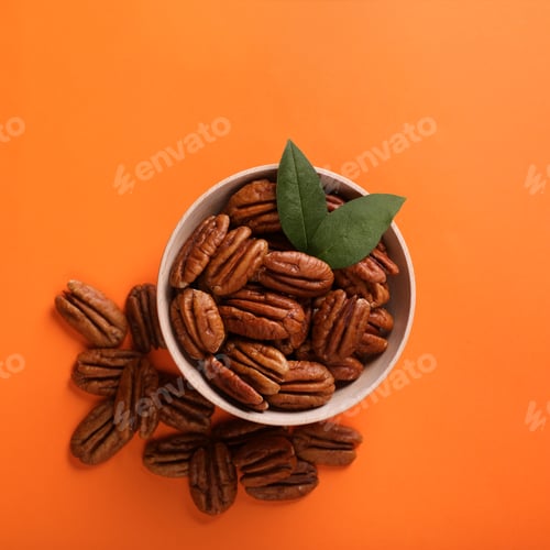 Preview: Bowl with tasty pecan nuts and green leaves on orange background, flat lay