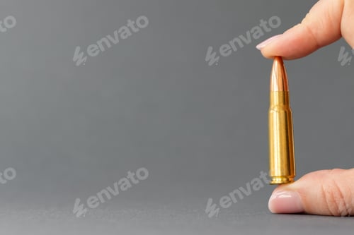 Preview: Hand with bullet on gray background. Cartridge 7.62 caliber for Kalashnikov assault rifle in fingers
