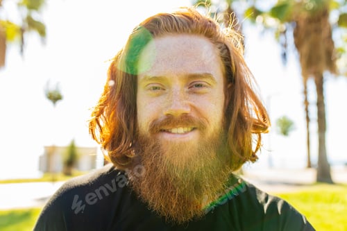 Preview: handsome redhaireb man with long beard wear black sporty suit and warming up in sunny beach