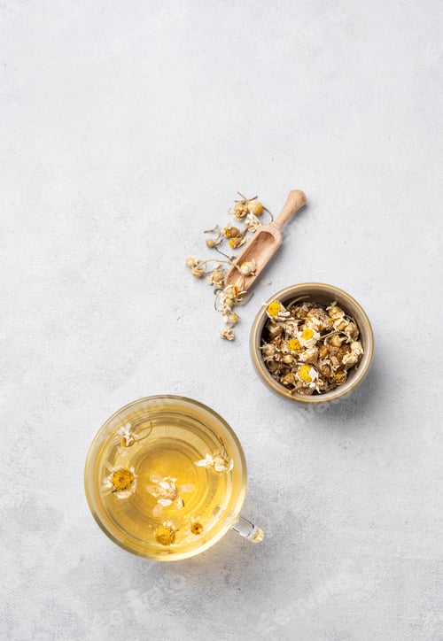 Preview: Chamomile herbal tea in a glass cup on a light background with dry flowers.