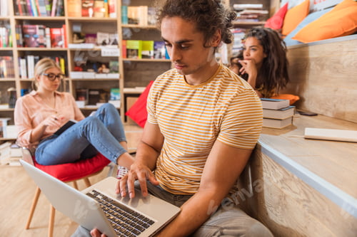 Preview: Portrait of young male student study in the library using laptop for researching online.
