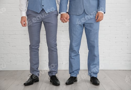 Preview: Newlywed gay couple holding hands near brick wall indoors